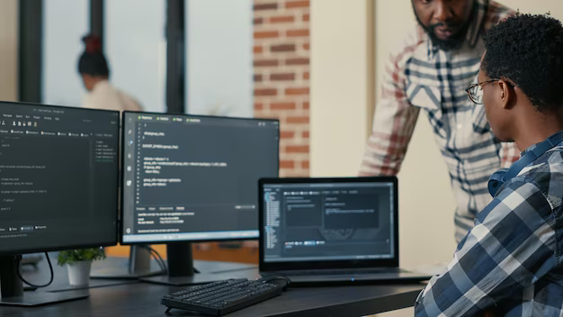 The programmer looks at three monitors on which program codes