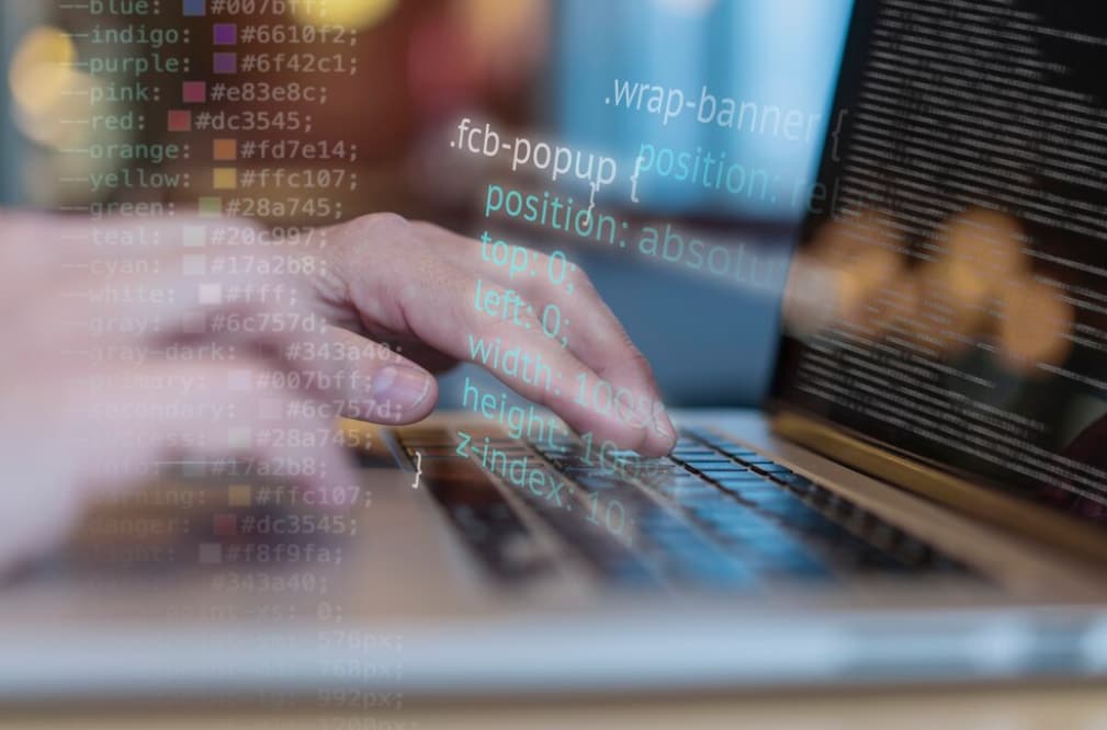 A person typing on a laptop with code overlay and bokeh effect