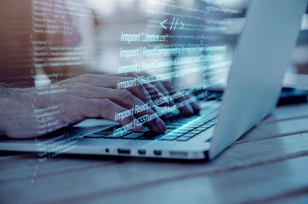 a side view of hands typing on the laptop keyboard, digital blue coding language above