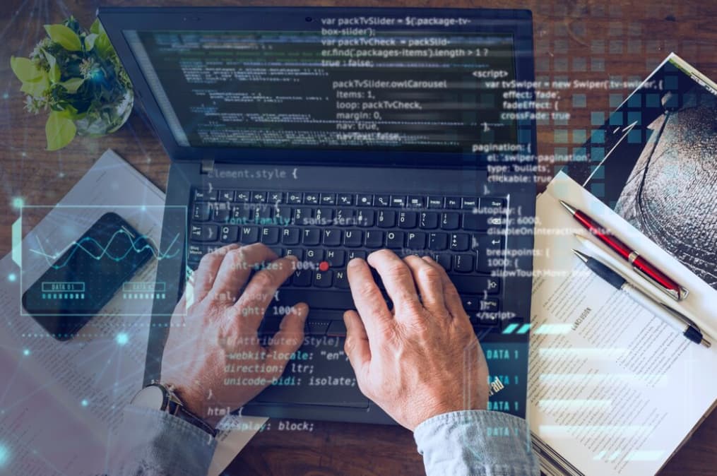 Close-up of hands typing on laptop with screen showing code